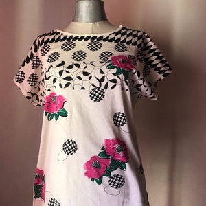 May include: White short-sleeved shirt with a black and white geometric pattern and pink flowers.