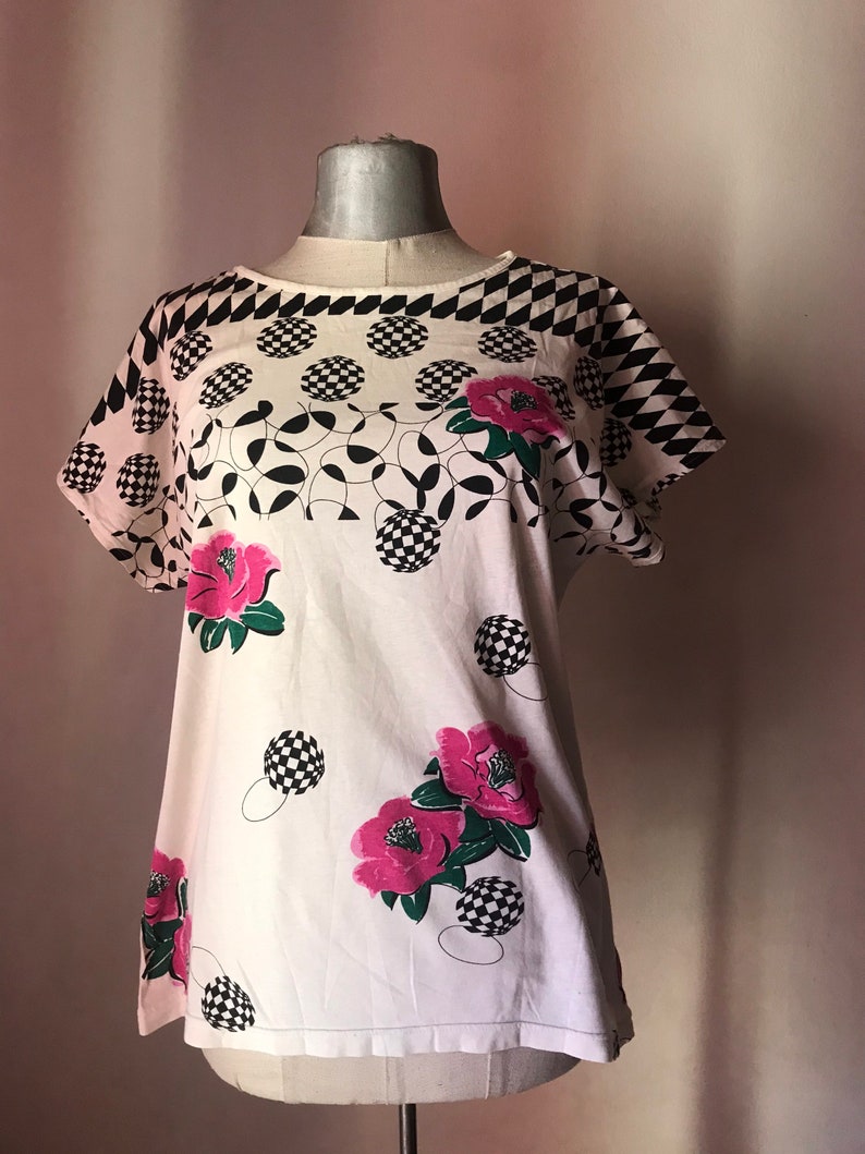 May include: White short-sleeved shirt with a black and white geometric pattern and pink flowers.