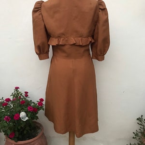 May include: A brown dress with a ruffled collar and sleeves. The dress has a fitted bodice and a flared skirt.