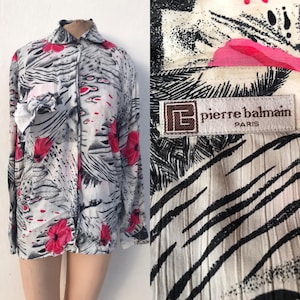 May include: A vintage button-down shirt with a floral and zebra stripe pattern. The shirt features red flowers and a white bow. The label reads "pierre balmain PARIS".