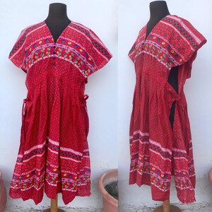 May include: A red cotton dress with a floral print and a V-neckline. The dress has short sleeves and a tie at the waist.