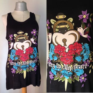 Op de afbeelding: Zwart tanktop met een grafische print van een hart met een sleutelgat, bloemen en een dolk. De tekst "key to my heart" is gedrukt op de voorkant van het shirt.