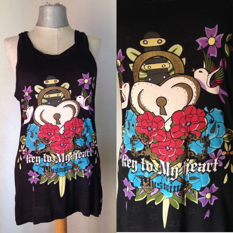 Op de afbeelding: Zwart tanktop met een grafische print van een hart met een sleutelgat, bloemen en een dolk. De tekst "key to my heart" is gedrukt op de voorkant van het shirt.