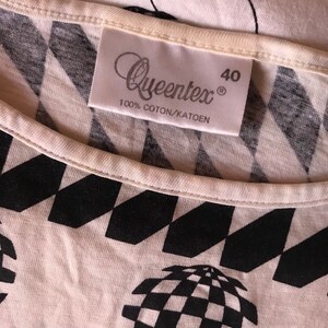 May include: White t-shirt with a black and white geometric pattern. The shirt has a label that says "Queentex" and "100% Coton/Katoen" and the size "40".