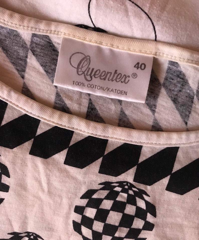 May include: White t-shirt with a black and white geometric pattern. The shirt has a label that says "Queentex" and "100% Coton/Katoen" and the size "40".