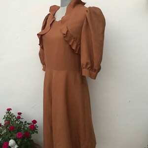 May include: A brown vintage dress with a ruffled neckline and puffed sleeves. The dress has a fitted bodice and a flowing skirt.