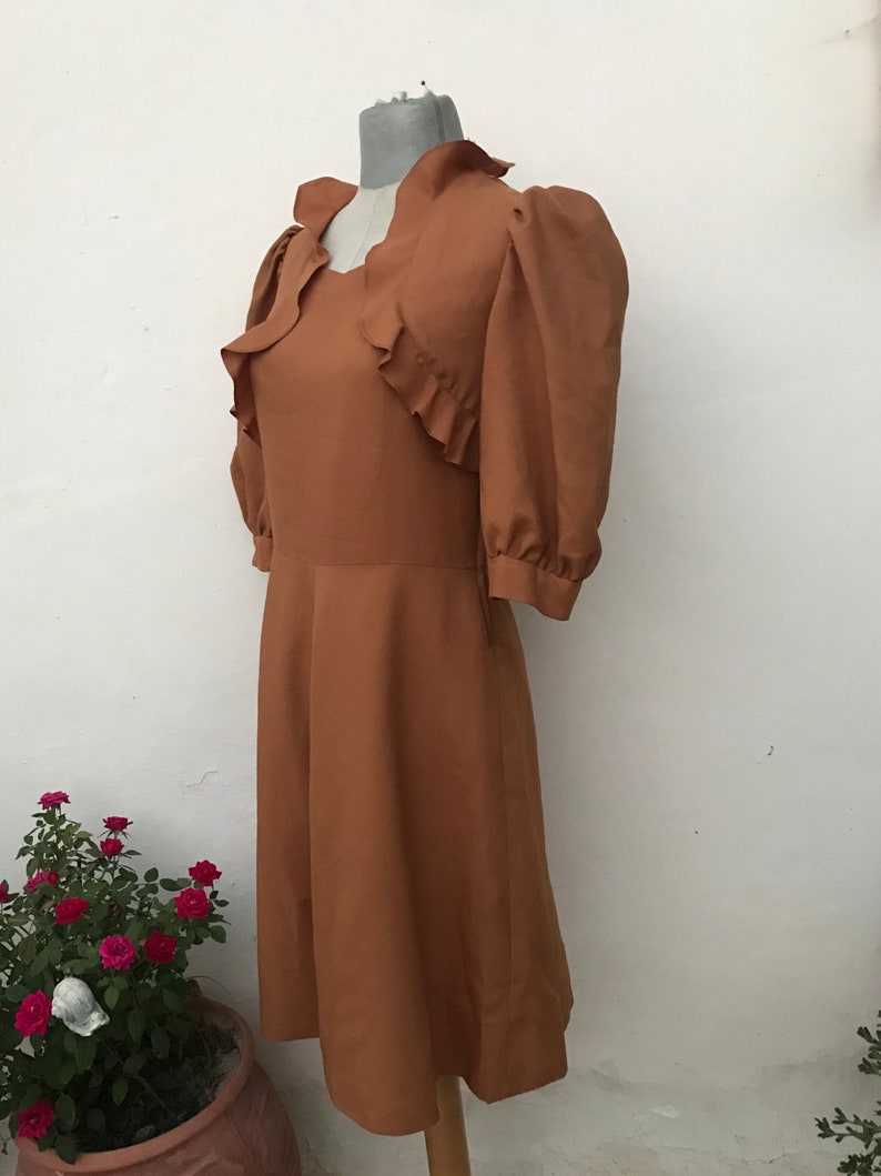 May include: A brown vintage dress with a ruffled neckline and puffed sleeves. The dress has a fitted bodice and a flowing skirt.