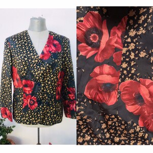 Op de afbeelding: Een zwarte blazer met een rode klaproos bloemenprint op een zwarte achtergrond. De blazer heeft een v-hals en lange mouwen.