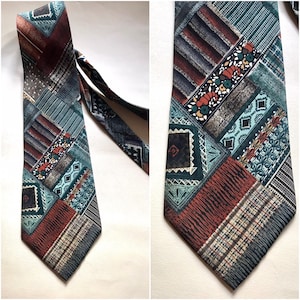 Puede incluir: Una corbata estampada con un diseño de patchwork en tonos marrones, verde azulado y naranja. La corbata presenta formas geométricas y motivos florales.