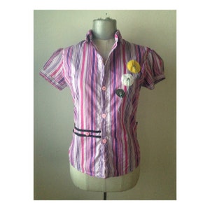 Puede incluir: Una camisa de manga corta a rayas rosa y morada con ribete negro y flores de tela de colores.