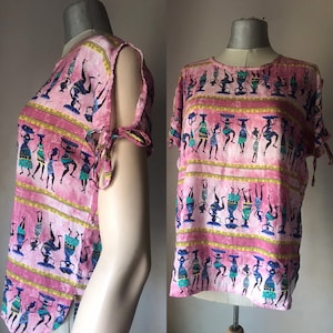 Puede incluir: Camiseta de manga corta rosa y blanca con un detalle de nudo en los hombros. La camiseta presenta un estampado colorido de figuras bailando con acentos azules, verdes y amarillos.