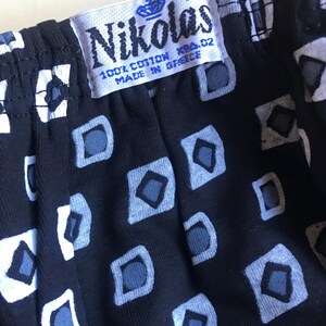 May include: A black and white patterned fabric with a white tag that says "Nikolas 100% Cotton Made in Greece" and a size tag that says "XL".