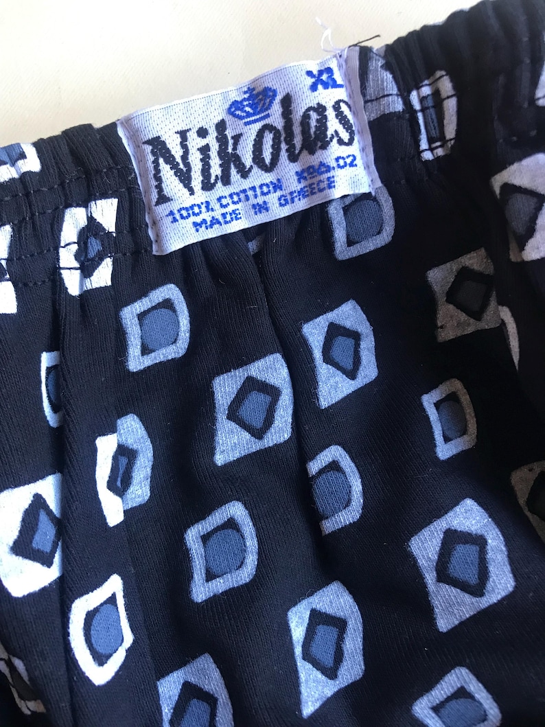 May include: A black and white patterned fabric with a white tag that says "Nikolas 100% Cotton Made in Greece" and a size tag that says "XL".