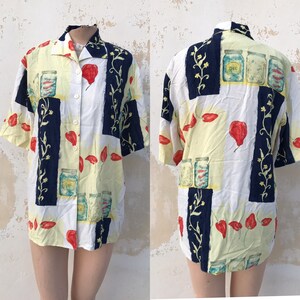 Op de afbeelding: Een wit en geel overhemd met korte mouwen en knopen met een blauwe, rode en groene print van potten en pepers.