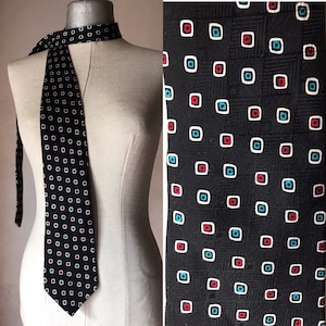 Op de afbeelding: Een zwarte zijden stropdas met een geometrisch patroon van rode, blauwe en witte vierkanten.