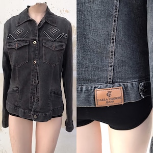 May include: A black denim jacket with a studded diamond pattern on the front and a brown leather patch on the back that reads "Carla Ferroni Jeans".