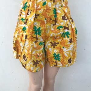 Könnte beinhalten: Hoch taillierte Shorts mit einem leuchtend gelben Hintergrund und einem kräftigen, abstrakten Blumenmuster in Grün-, Braun- und Weißtönen. Das Kleidungsstück verfügt über vertikale Falten auf der Vorderseite und einen seitlichen Knopfverschluss.