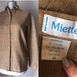 May include: A brown and white plaid long-sleeved shirt with a button-up front. The shirt has a label that reads "Miettes" and "Fabrique en France 50% Polyester 33% Laine 17% Lurex 40".