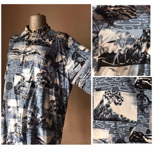 Può includere: Una camicia abbottonata blu e bianca con un design di ispirazione giapponese. La camicia presenta immagini di montagne, onde e alberi.
