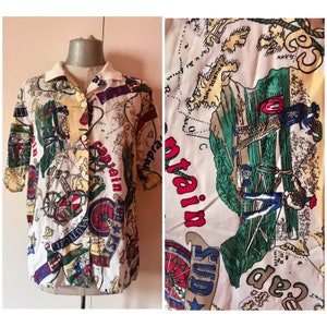 Blusa abotonada con cuello blanco vintage de los años 80 con estampado loco, presenta viajeros, barcos y diseños de letras identificables.