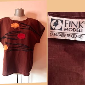 May include: A brown short-sleeved blouse with a floral design featuring orange, red, and yellow tulips. The blouse has a round neckline and a FINK MODELL label with size information: B 46, GB 18, F 48.