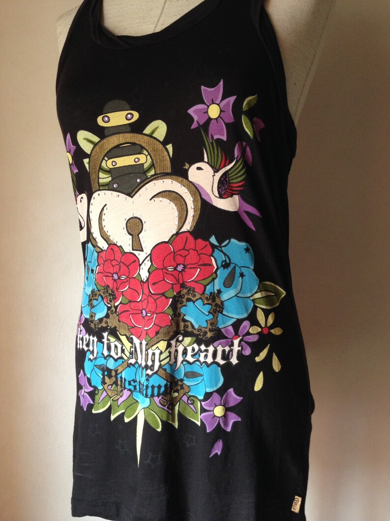 Op de afbeelding: Zwart tanktop met een kleurrijke grafische print van een hart met een sleutelgat, bloemen en een vogel. De tekst "key to my heart" is onder de print gedrukt.