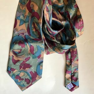 Peut inclure: Une cravate à motifs avec un motif répété de formes sarcelle, bordeaux et beige. La cravate est faite d'une matière soyeuse et est nouée. L'étiquette au bout de la cravate porte les chiffres "020 729".