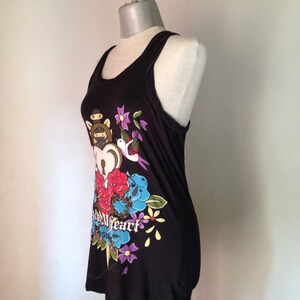 Op de afbeelding: Zwart tanktop met een kleurrijke grafische print van een hart, bloemen, een vogel en een dolk. De tekst "Wild Heart" is op de print gedrukt.
