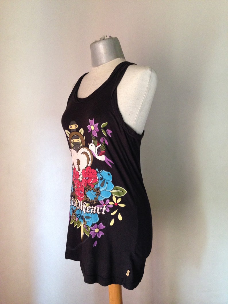 Op de afbeelding: Zwart tanktop met een kleurrijke grafische print van een hart, bloemen, een vogel en een dolk. De tekst "Wild Heart" is op de print gedrukt.