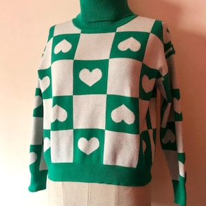 緑の草と白のタートルネックのクロップド丈セーター。四角とハートが特徴で、90年代風に70年代風にアレンジされたオールドスクールなデザイン。