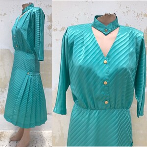 May include: A teal blue dress with a diagonal stripe pattern. The dress has a high neckline with a keyhole opening and a button-up front. The dress has 3/4 sleeves and a pleated skirt.