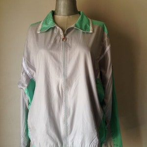 Puede incluir: Chaqueta deportiva vintage gris y verde menta con cierre de cremallera completo. La chaqueta presenta un cuello y detalles de manga blancos, y un dobladillo y pu&ntilde;os verde menta. La chaqueta se muestra en un maniqu&iacute;.