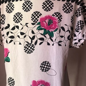 May include: White t-shirt with a black and white checkered pattern at the top, followed by a pattern of black and white checkered circles and pink flowers.