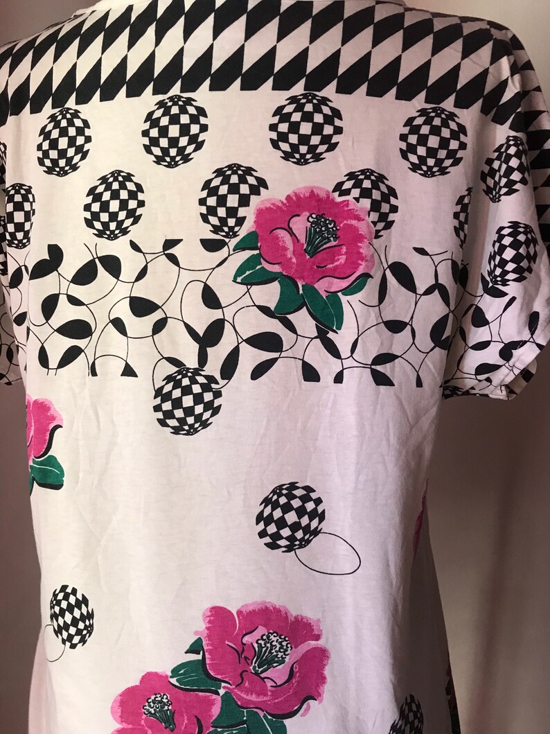 May include: White t-shirt with a black and white checkered pattern at the top, followed by a pattern of black and white checkered circles and pink flowers.