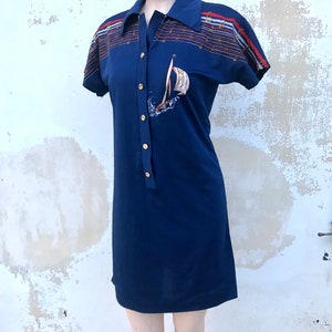 May include: A navy blue short-sleeved dress with a white sailboat graphic and a striped collar. The dress has gold buttons down the front.
