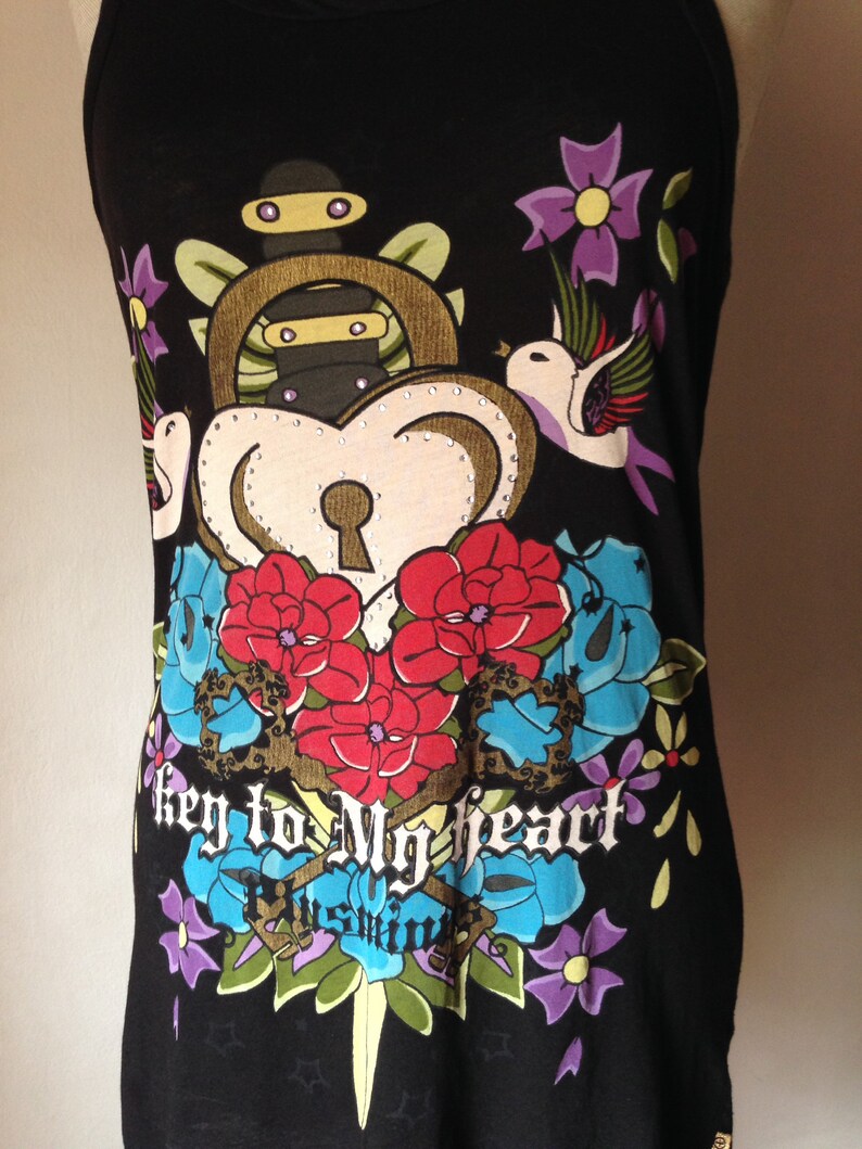 Op de afbeelding: Zwart tanktop met een kleurrijke grafische print van een hart met een sleutelgat, een hangslot, een dolk en bloemen. De tekst "key to my heart" is gedrukt op de voorkant van het tanktop.