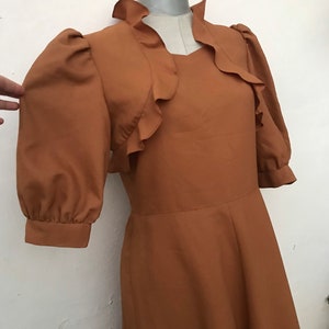 May include: A brown dress with a ruffled neckline and puffed sleeves. The dress has a fitted bodice and a flowing skirt.