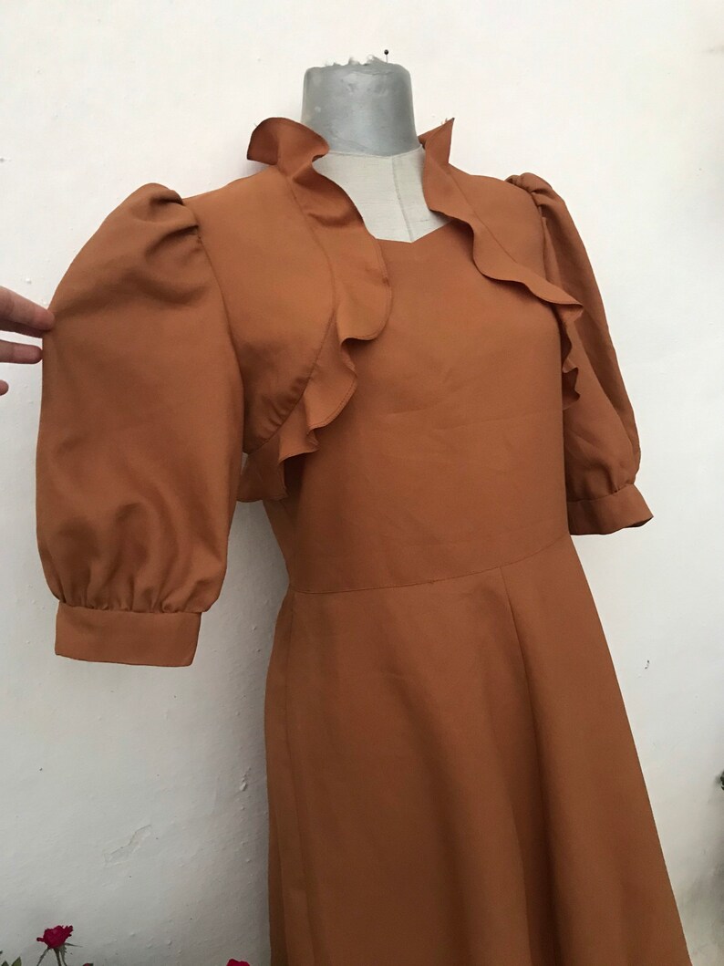 May include: A brown dress with a ruffled neckline and puffed sleeves. The dress has a fitted bodice and a flowing skirt.