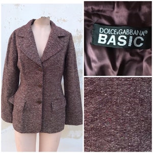 Può includere: Un blazer in tweed marrone con colletto a revers, tre bottoni e due tasche. Il blazer ha un'etichetta che recita "Dolce & Gabbana® BASIC".