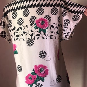 May include: White short-sleeved shirt with a black and white checkered pattern, pink flowers, and black and white circles.