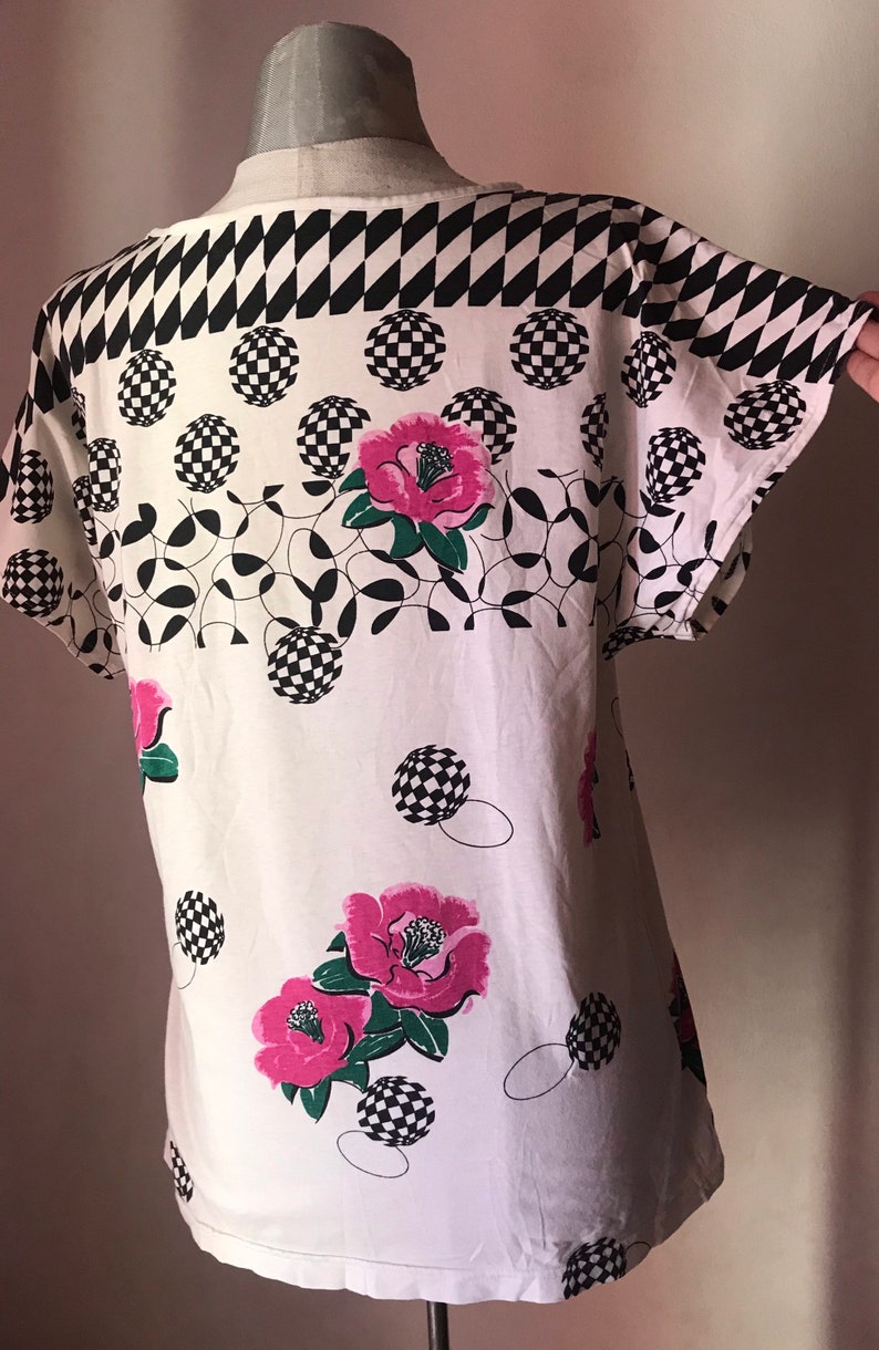 May include: White short-sleeved shirt with a black and white checkered pattern, pink flowers, and black and white circles.