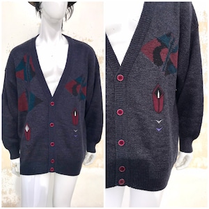 Puede incluir: Un cárdigan gris oscuro con un patrón geométrico en tonos de rojo, azul y verde. El cárdigan tiene cuello en V y cierre de botones.