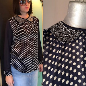 May include: A navy blue and white polka dot sheer blouse with a beaded collar. The blouse has long sleeves and a peter pan collar.