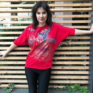 Röd 80-tals vintageblus med glamorös guldblå design framtill, en anka som flyger över en damm med vass, fladdermusvingar i ärmarna och axelvaddar