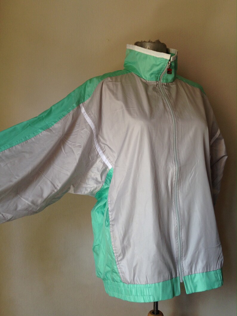 Puede incluir: Chaqueta deportiva vintage en gris, verde menta y blanco. La chaqueta tiene un cuello alto, una cremallera completa y pu&ntilde;os y dobladillo el&aacute;sticos. Las mangas y los laterales est&aacute;n acentuados con paneles verde menta y rayas blancas.