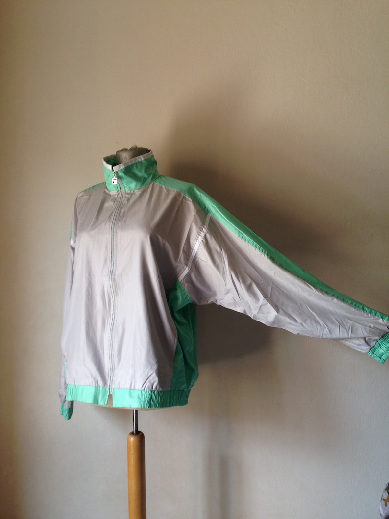 Puede incluir: Chaqueta deportiva gris y verde menta con cierre de cremallera completo. La chaqueta tiene cuello alto y pu&ntilde;os y dobladillo el&aacute;sticos. Las mangas y los paneles laterales son verde menta, el cuerpo es gris.