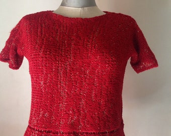 May include: A red knitted sweater with a sparkly texture and short sleeves. The sweater has a round neckline and a slightly flared hem.