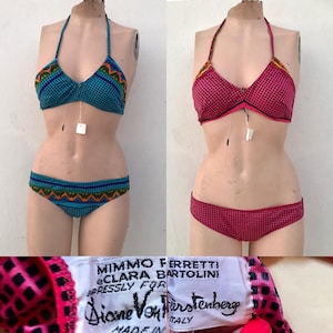 May include: Two two-piece bikinis on mannequins. One is teal with a blue dot pattern and orange-green geometric trim. The other is pink with a black grid pattern and orange-yellow trim. A white fabric tag reads Mimmo Ferretti e Clara Bartolini expressly for Diane Von Furstenberg.