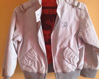 May include: A light gray bomber jacket with a zipper closure and a skull graphic on the right side. The jacket has a gray ribbed collar, cuffs, and hem. The lining is red and features a graphic of a guitar and the text "Full Paul".