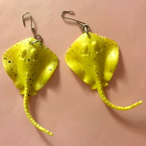 Könnte beinhalten: Ein Paar gelbe Rochen-Ohrringe mit schwarzen Punkten. Die Ohrringe sind aus Kunststoff und haben silberne Haken.